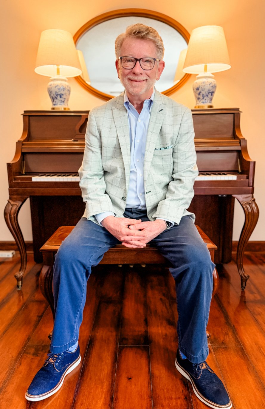 Paul Raddin, Lead Instructor, seated at an upright piano